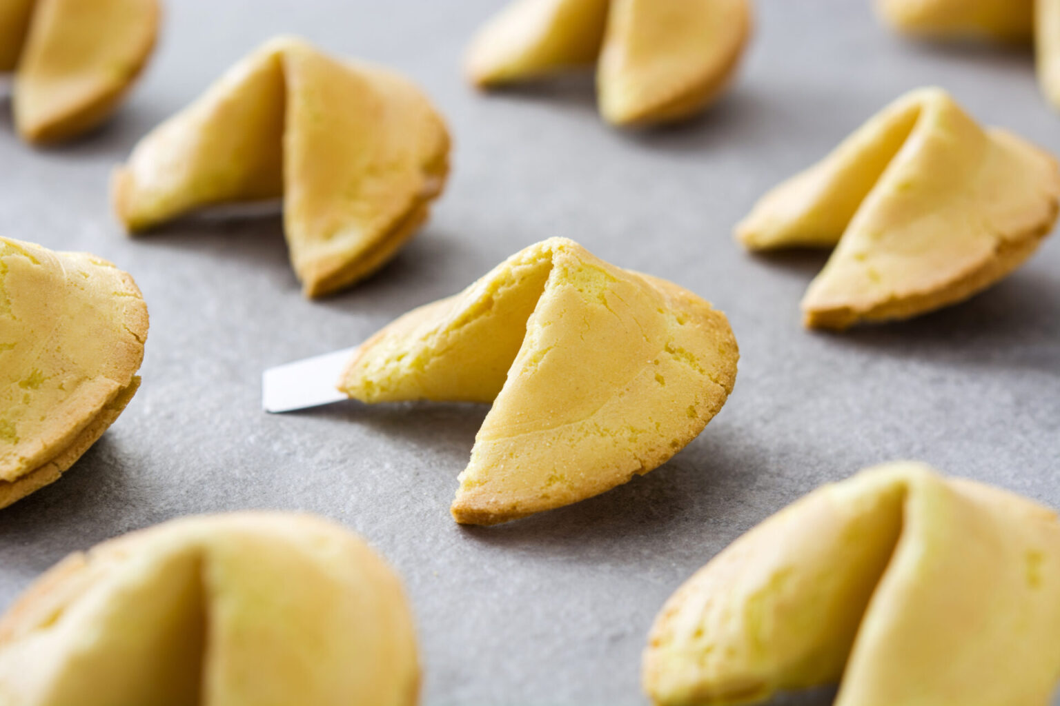 Homemade fortune cookies with fortune peeking out on a grey surface
