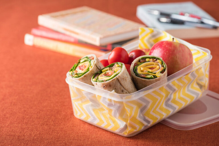 Pinwheel sandwiches in a lunchbox with colourful napkin and apple