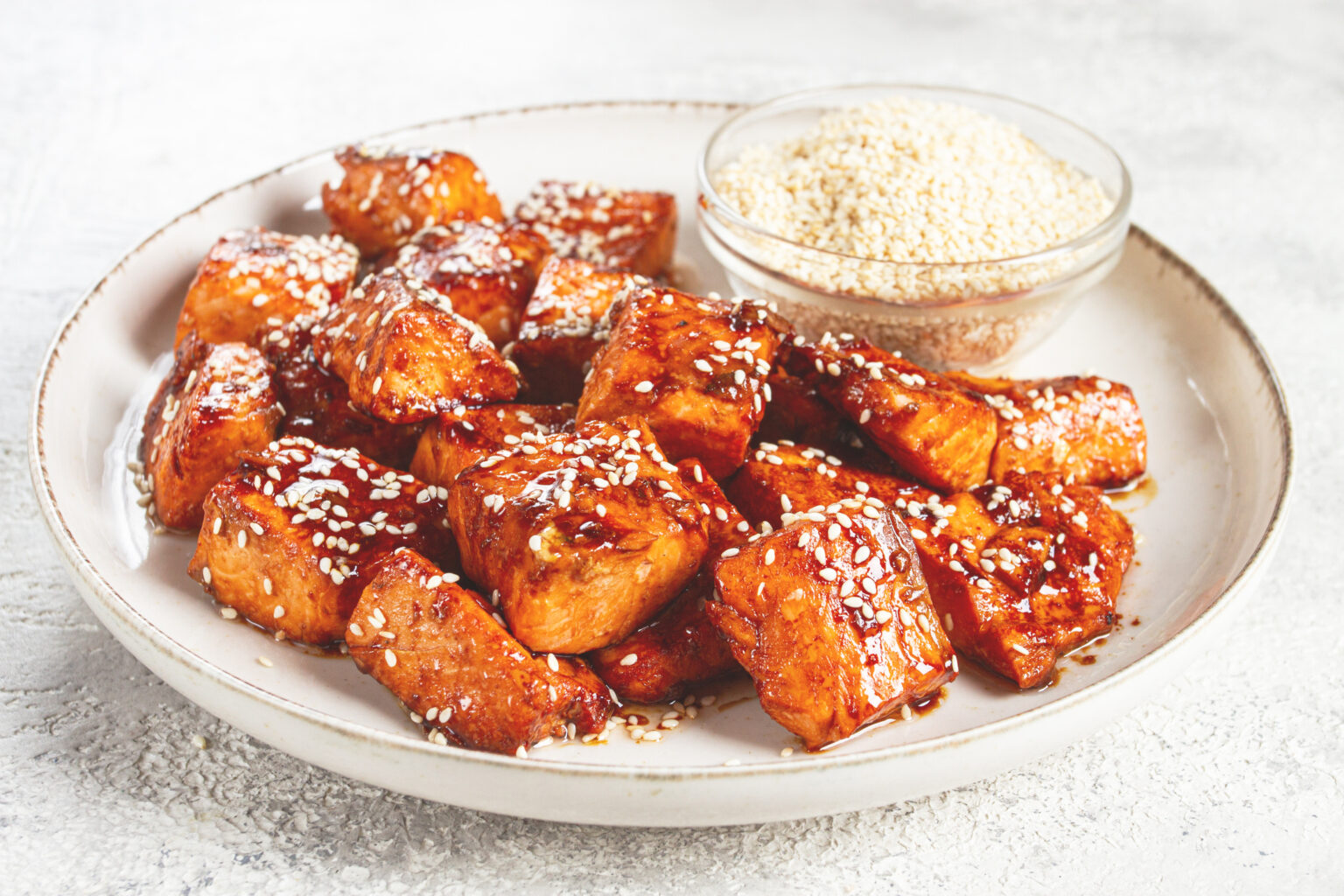 Maple sesame salmon bites on a white plate with dipping sauce