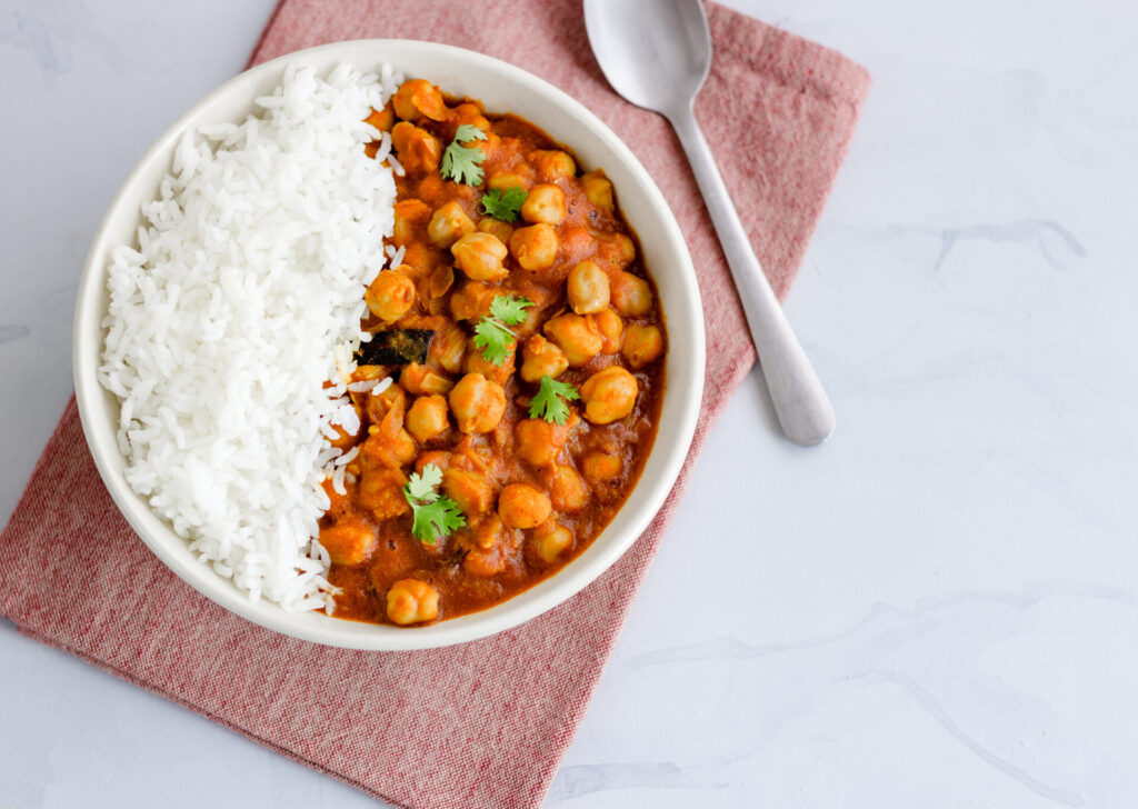 Chickpea, mushroom and chicken thigh curry in a white bowl with rice