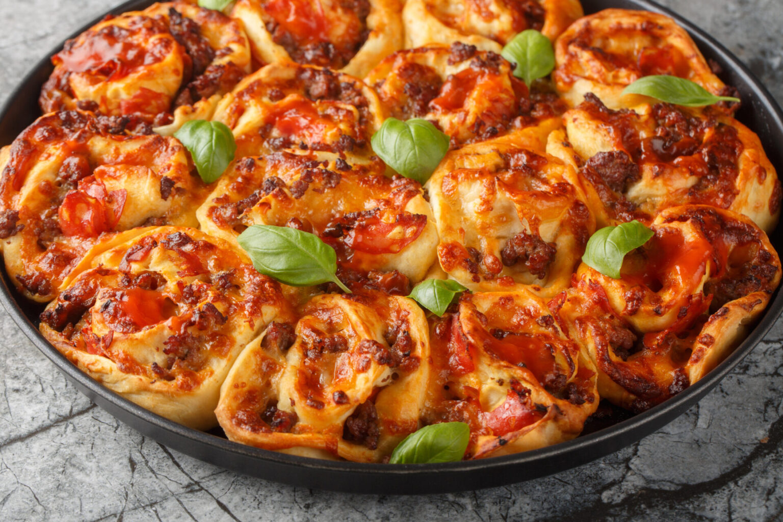 Pull-apart pizza with tomato sauce, cheese and basil in a cast iron pan