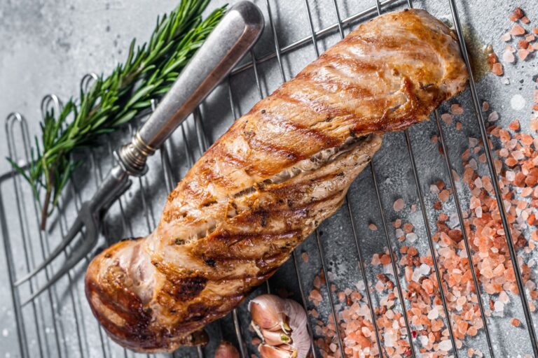 Grilled pork tenderloin on a cooling rack with aromatics