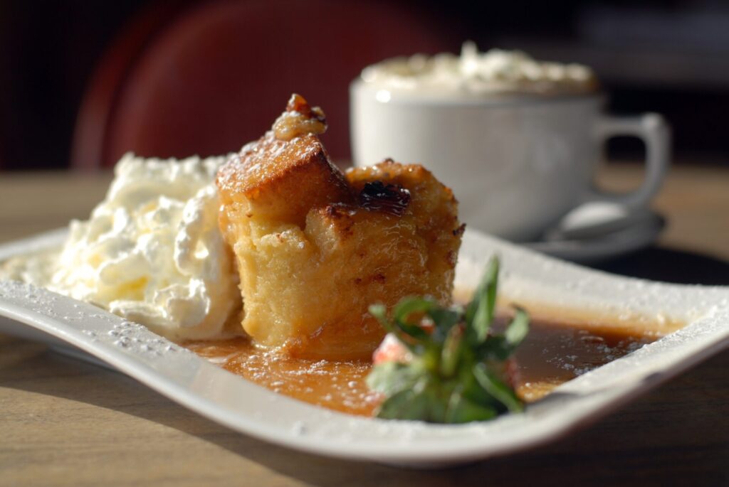 Cinnamon-apple bread pudding with whipped cream on white serving plate