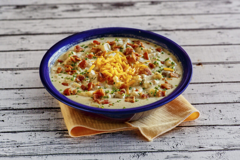 Baked potato soup with toppings in a blue bowl, resting on an orange napkin