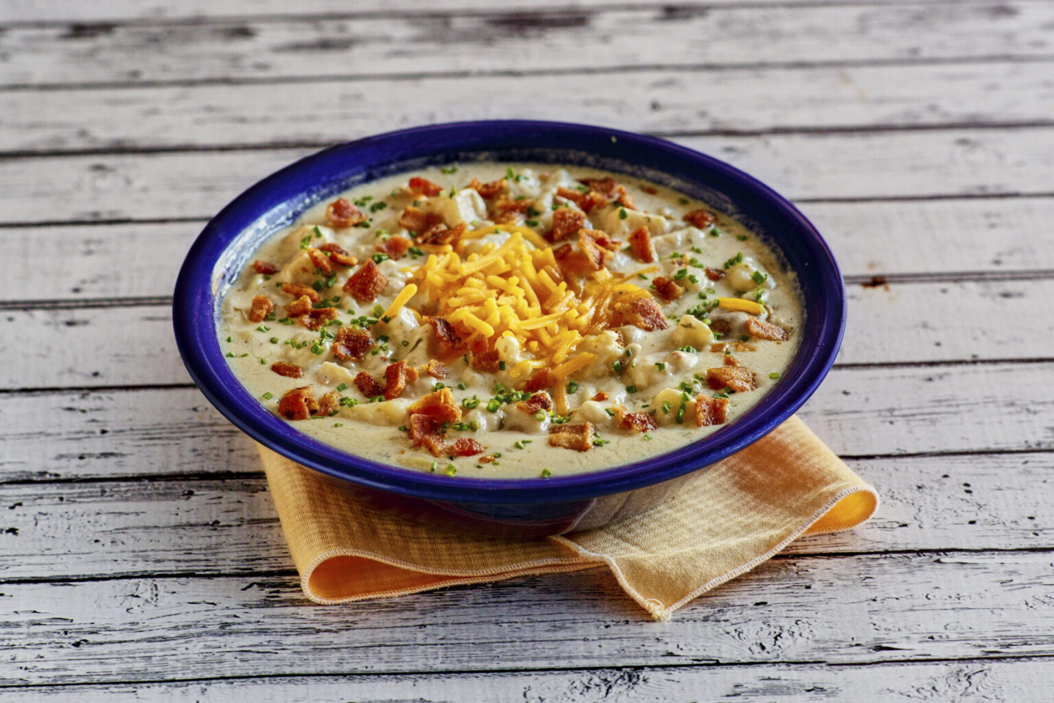 Baked potato soup with toppings in a blue bowl, resting on an orange napkin