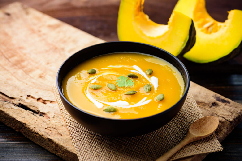 Butternut squash and pear soup in a black bowl, with pumpkin seeds and a swirl of cream