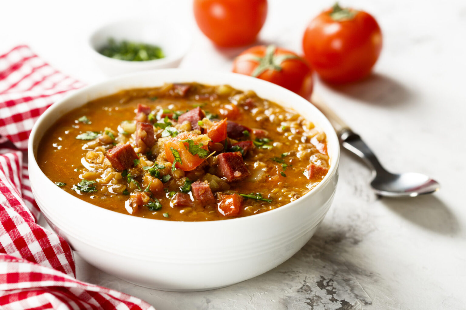 Sausage, Lentil and Barley Soup in a white bowl with a red gingham napkin