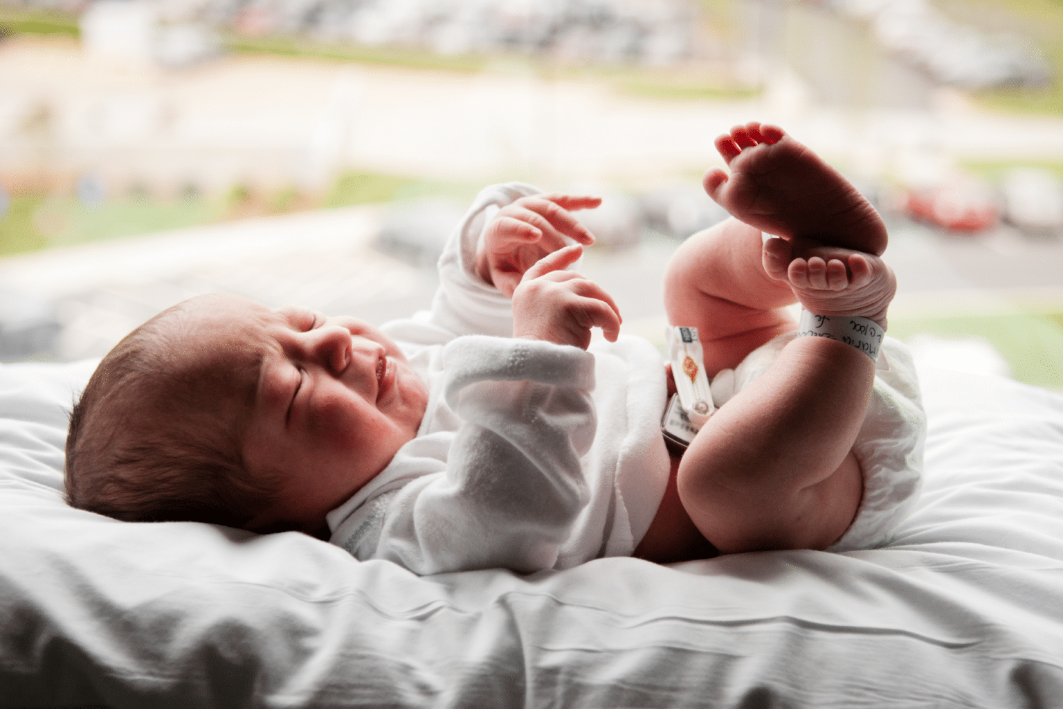 newborn baby laying on a sheet with his legs up