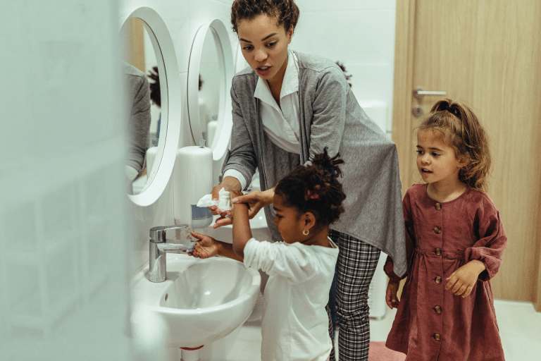 woman helping little girls wash their hands at a sink