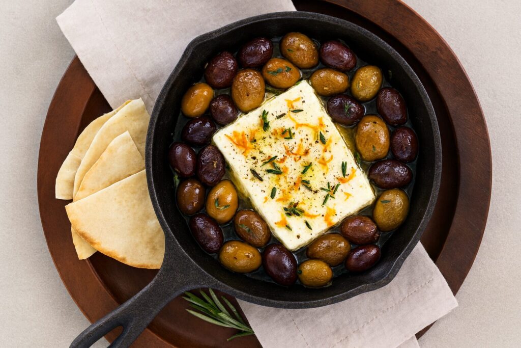 Roasted olives and feta in a black cast-iron skillet with a side of pita wedges