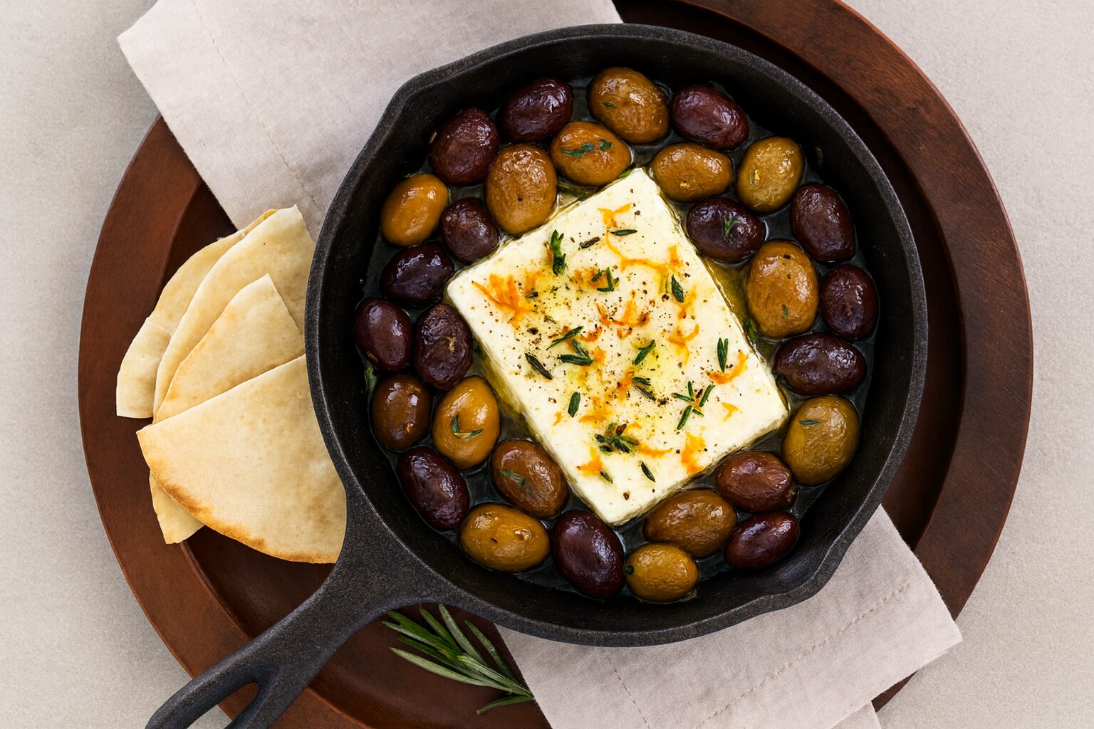 Roasted olives and feta in a black cast-iron skillet with a side of pita wedges