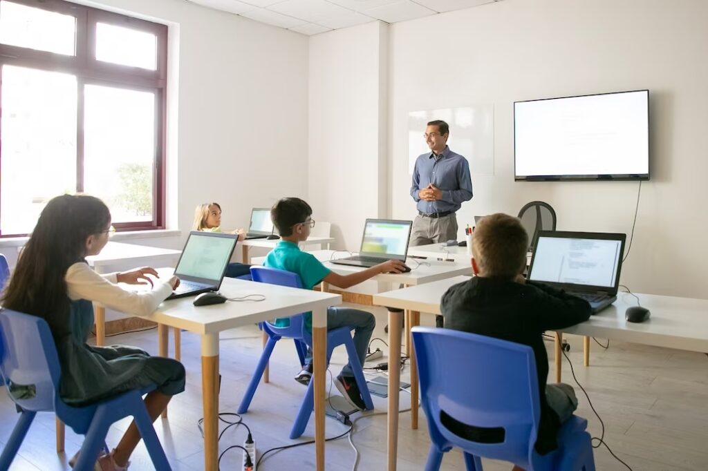 a man standing in front of a group of kids using laptops