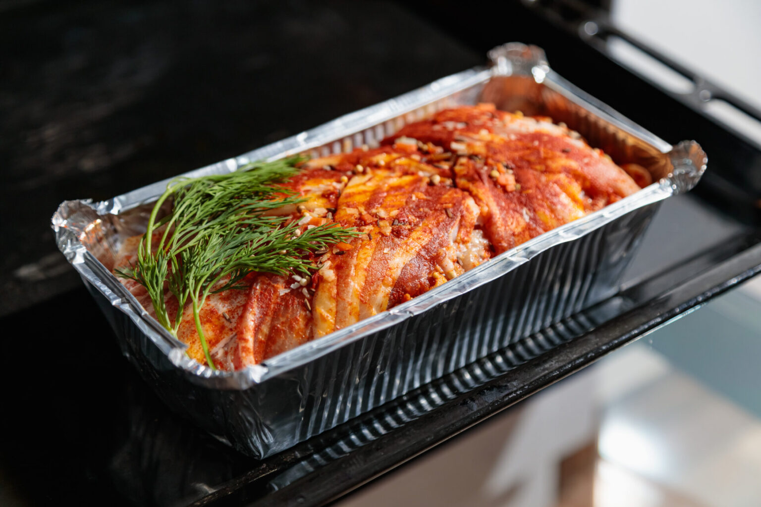 Bacon cheeseburger meatloaf in a metal cooking tin with herb garnish