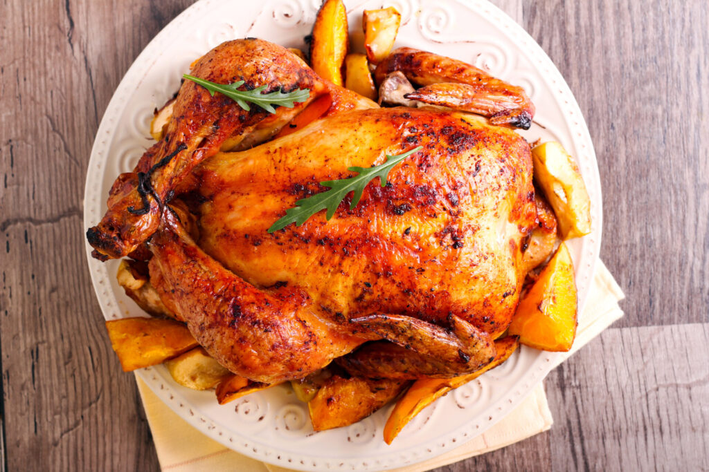 Whole roasted chicken with potatoes and vegetables on a pattern white plate