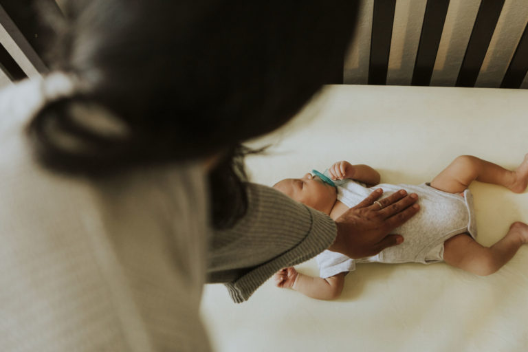 mother touching her baby's belly as he sleeps in crib