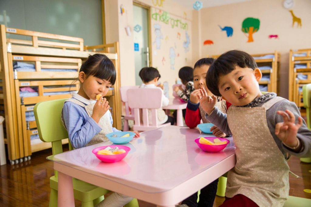 Three children sitting at a white table eating