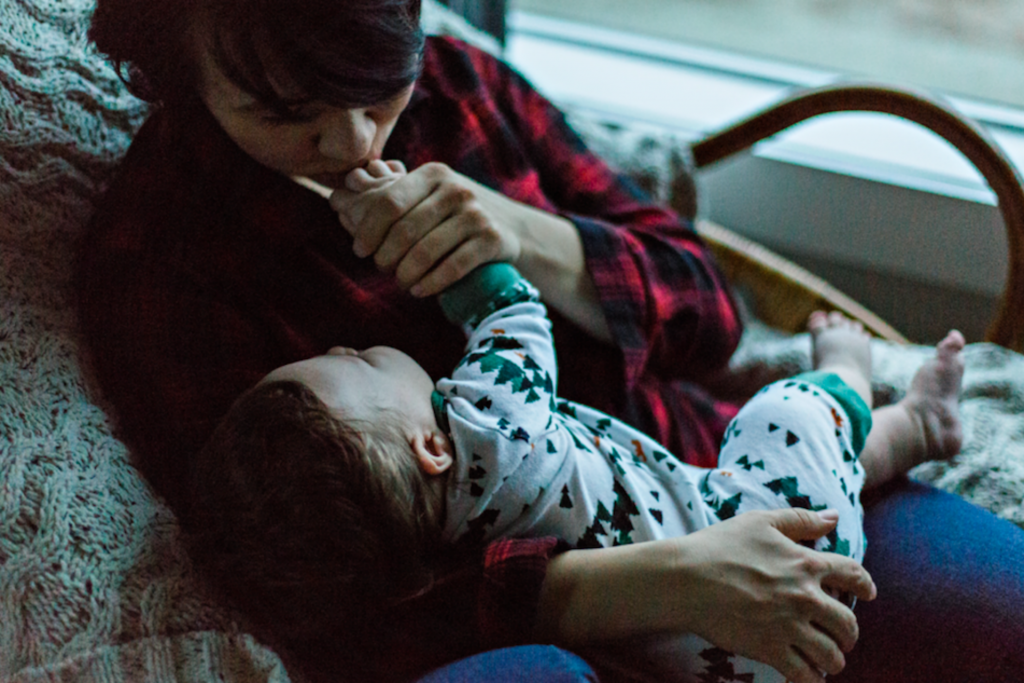 mother holding her toddler and kissing his hand