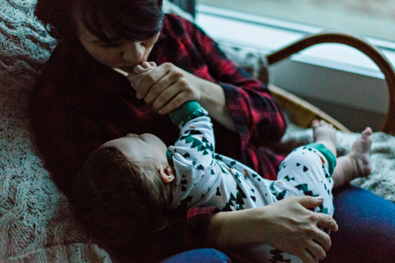 mother holding her toddler and kissing his hand