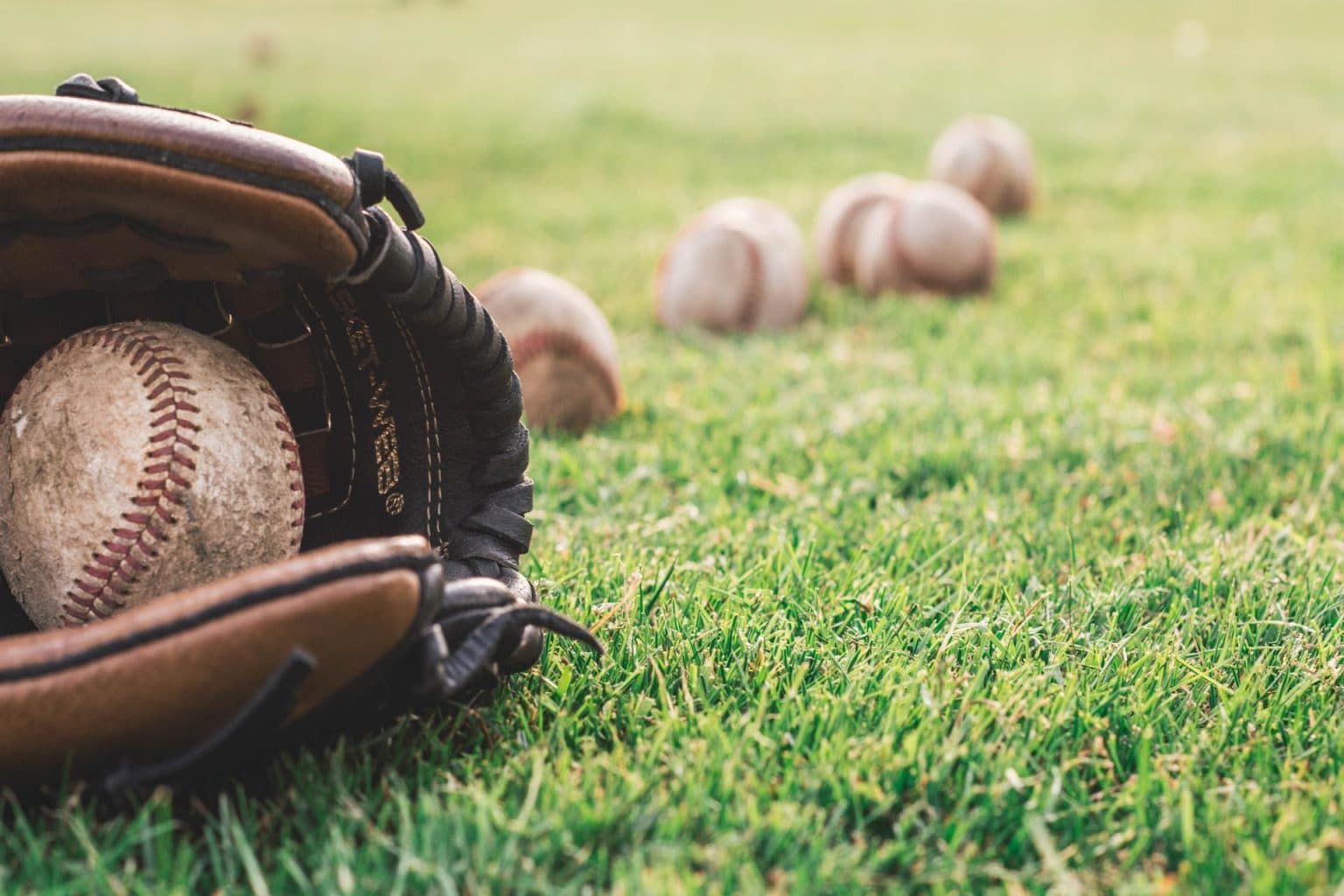 Baseball glove and baseballs lying in the grass