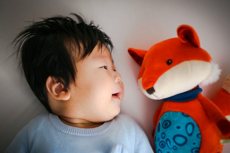 baby laying down next to a stuffed animal