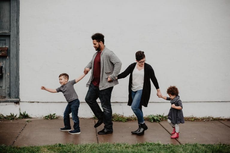 A family hold hands as they walk down a street, illustrating the idea that parenting is harder than ever before