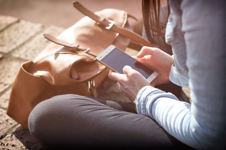 Girl looking down at phone, sitting in front of knapsack