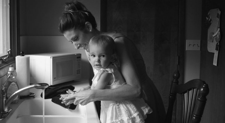 Black-and-white image of mom and child washing hands at a sink