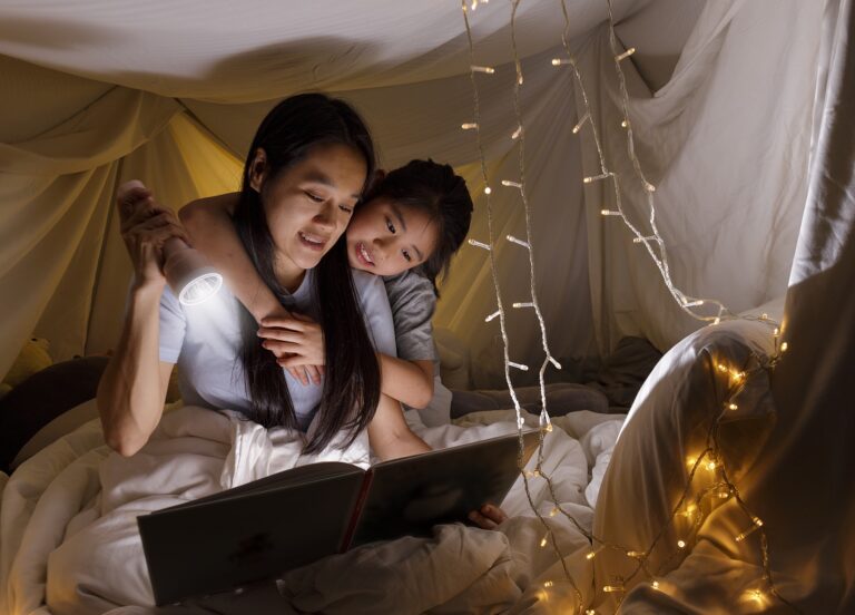 Mother and child reading awesome picture books by flashlight, with twinkle lights all around