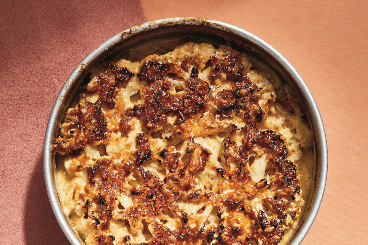 cheesy roasted cauliflower on a pink-hued background