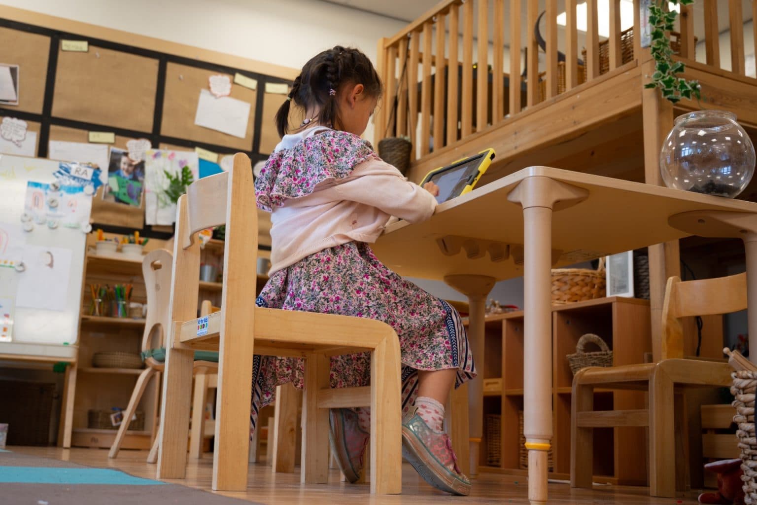 little girl sits at a desk at school with a tablet