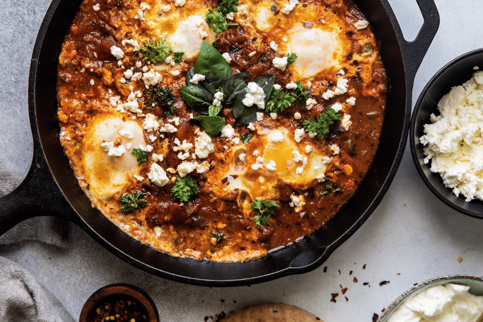 cast iron frying pan with shakshuka, feta cheese and pita bread