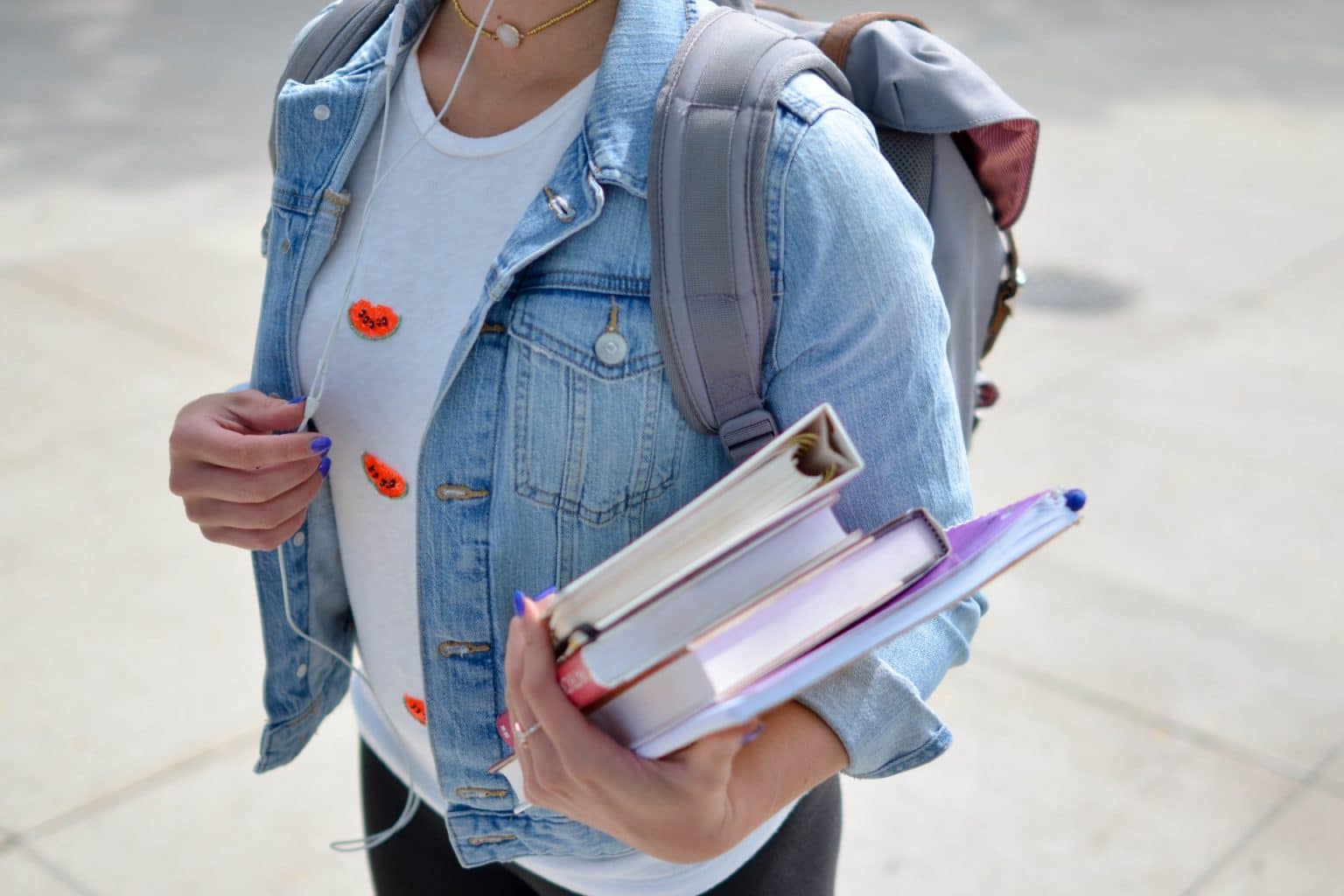 teen holding books with a jean jacket and headphones