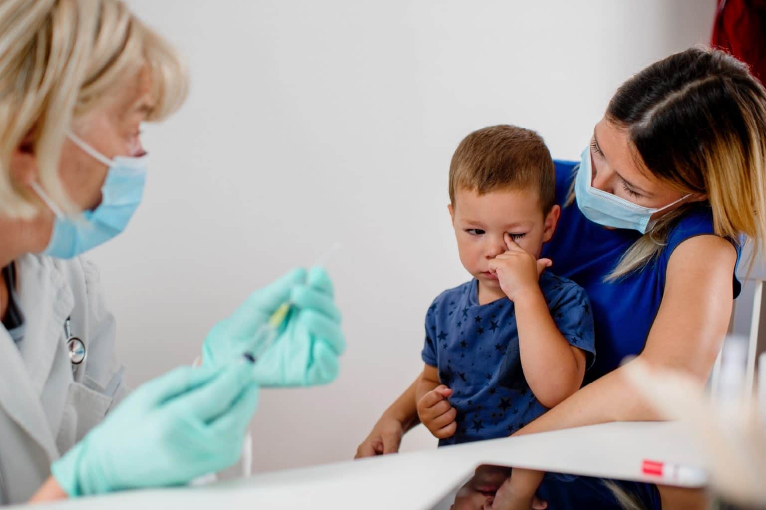 boy sits on his mother's lap to get a shot, he looks uneasy