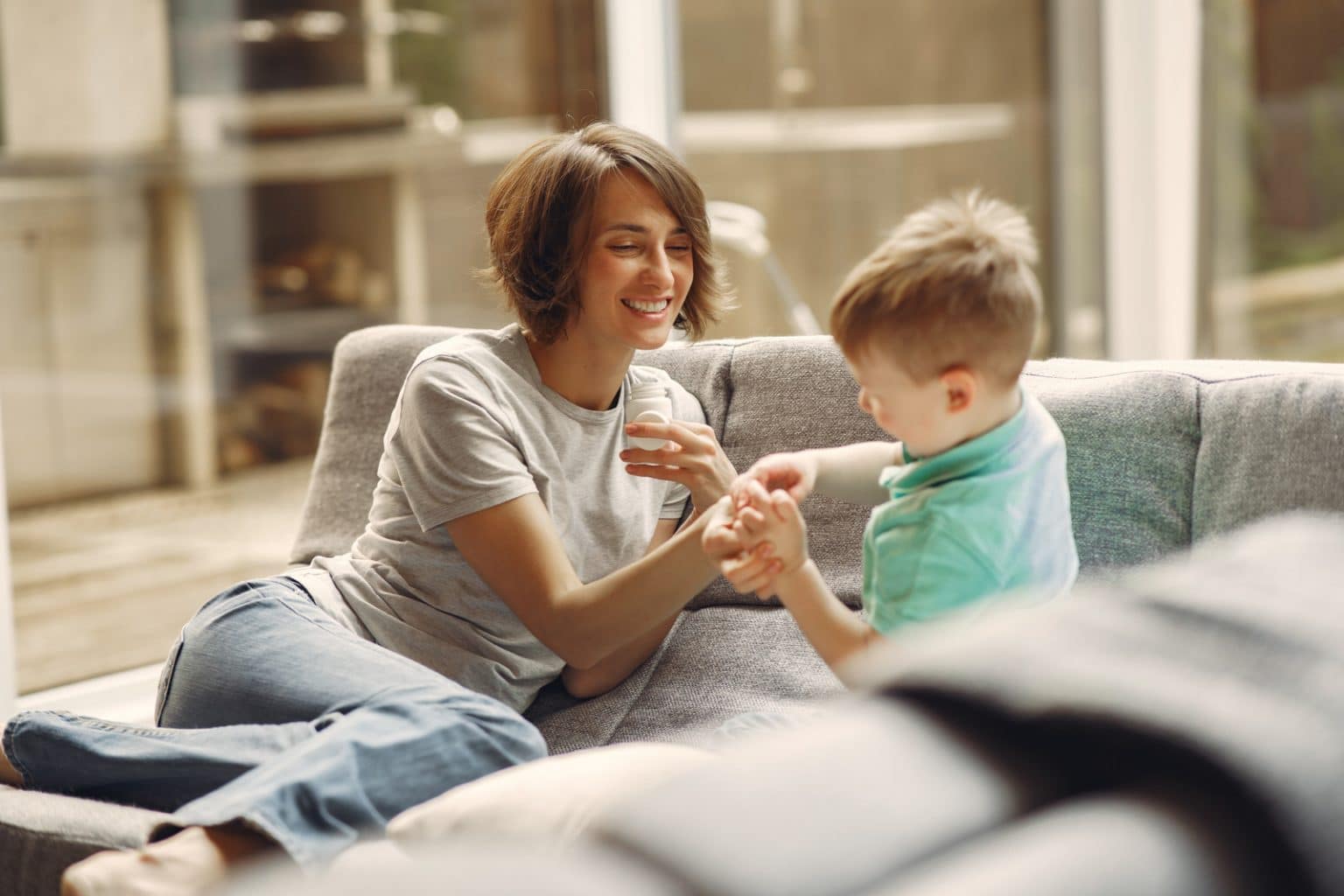 mom giving son medicine on the couch. Both are smiling