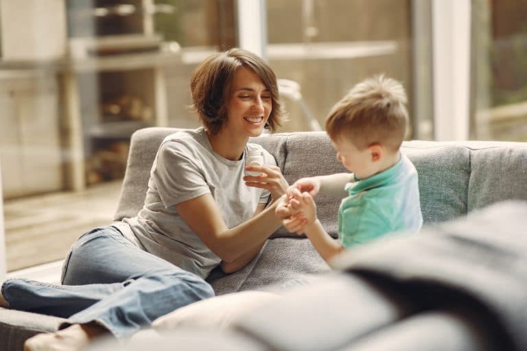 mom giving son medicine on the couch. Both are smiling