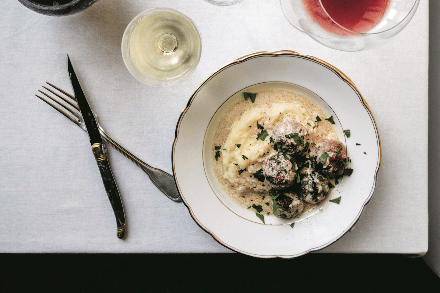 plate of meatballs in a creamy sauce on top of mashed potatoes and sprinkled with parsley