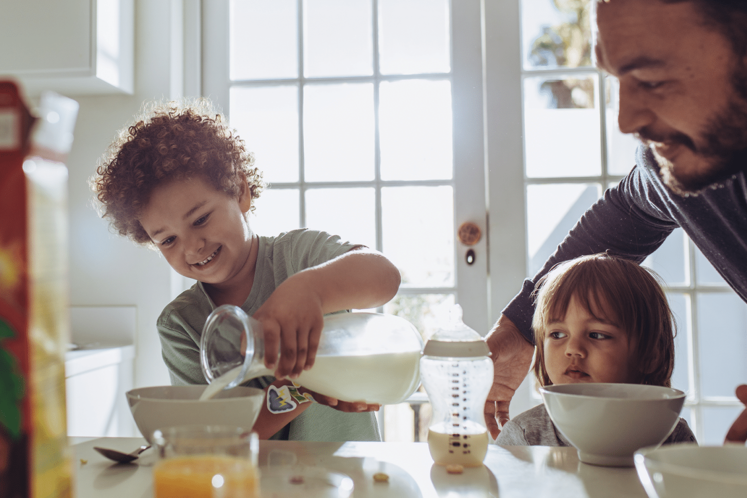 father and two children at the breakfast table pouring milk into bowls