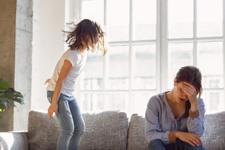 child jumps on the sofa stressing out mother who is sitting nearby