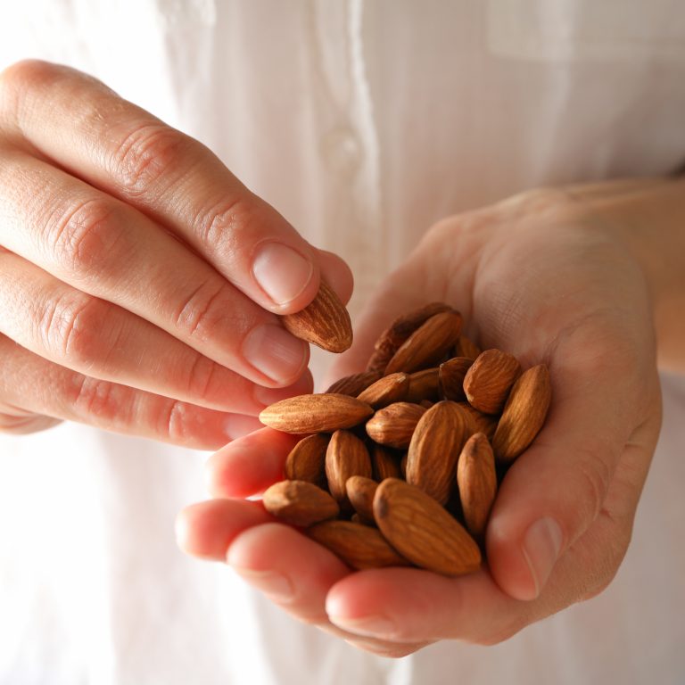 woman-presenting hands holds almonds against a white linen shirt