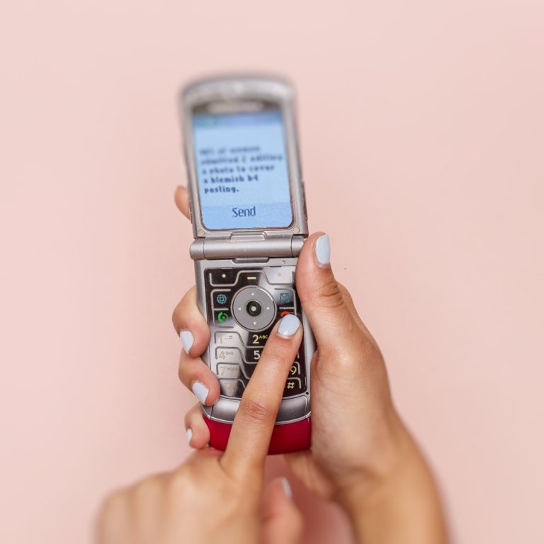 hands with light blue nail polish holding flip phone and texting with left index finger
