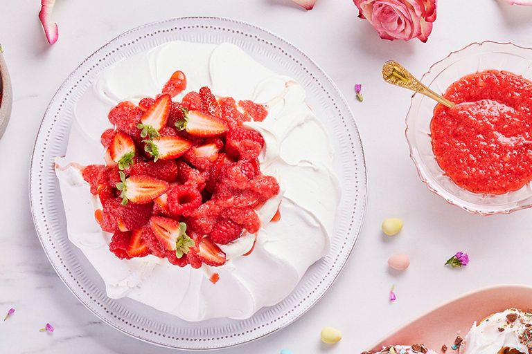 a pavlova topped with fresh fruit and chopped nuts