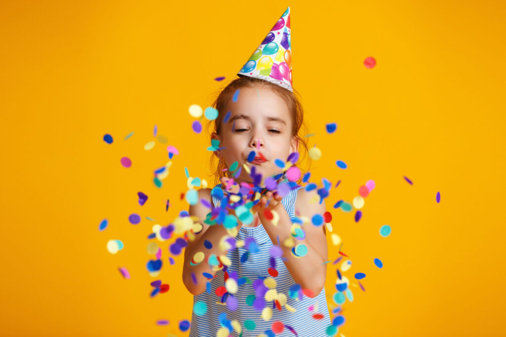 a girl blowing confetti in front of a yellow background