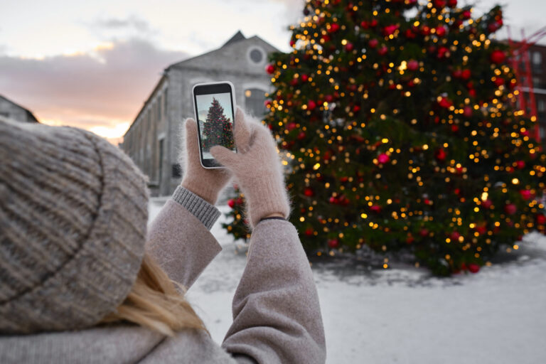 A woman takes a photo of a Christmas tree with her iPhone