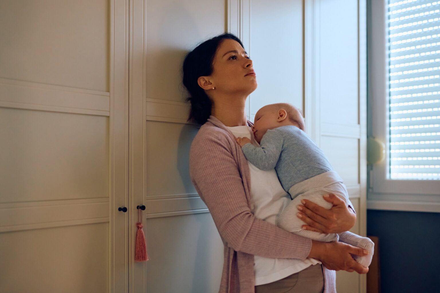 a mother holds her baby while looking sad and depressed