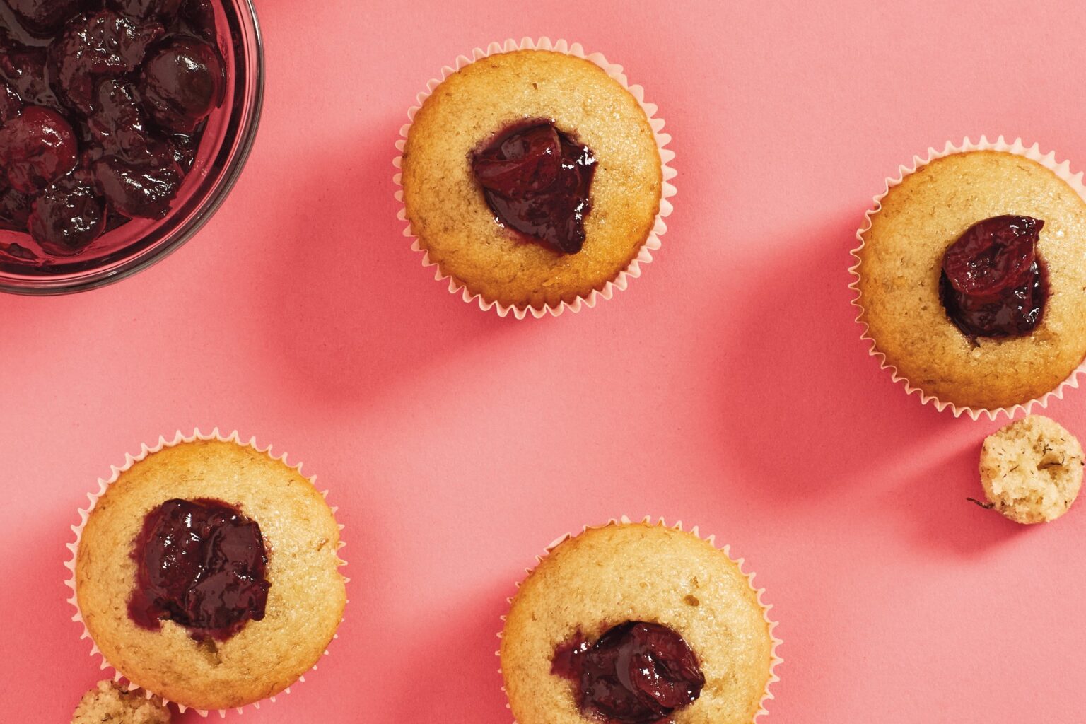 Banana cupcakes with cherry icing sit on a pink background