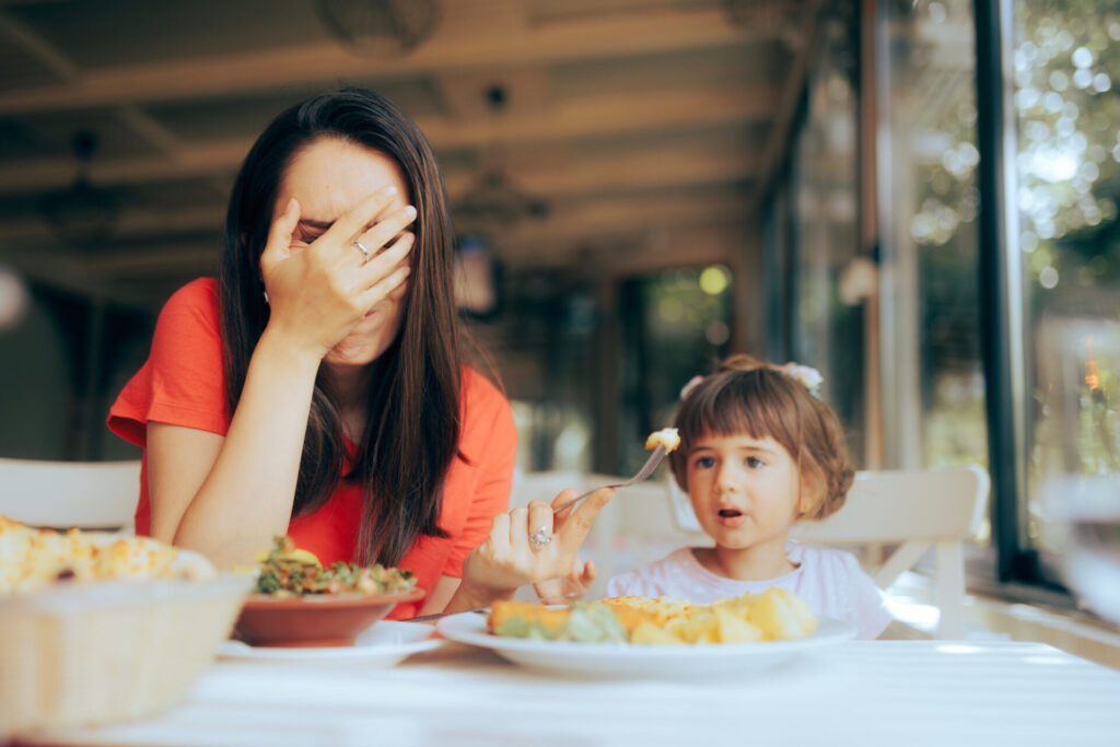 a woman covering her face with her hand while sitting at a table with food