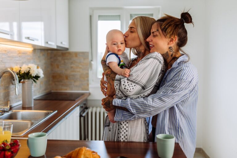 two mothers embrace while holding their toddler