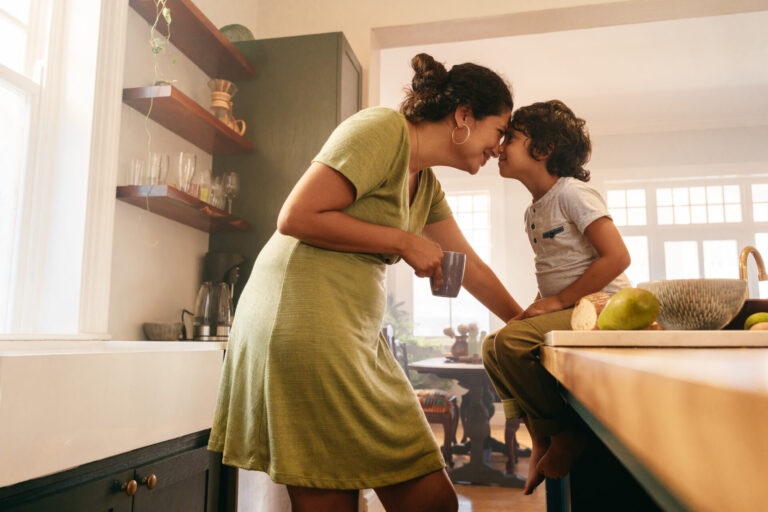 Mother nose to nose with a child, while drinking a cup of coffee in the kitchen