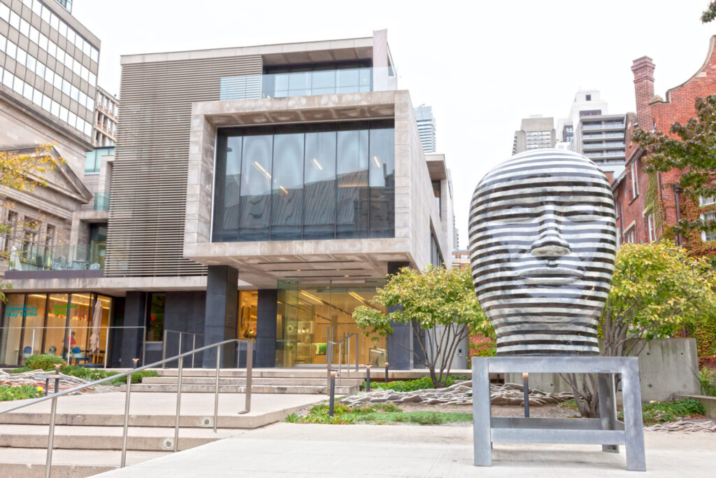 The Gardiner Museum entrance, with a large head statue at the front of the building, and green trees behind it.