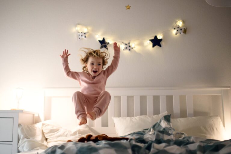 Child jumps on the bed in a dimly lit room seemingly avoiding bedtime